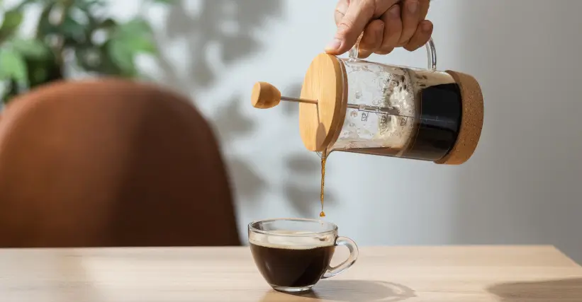 close em uma mão colocando o café de uma prensa francesa em uma xícara