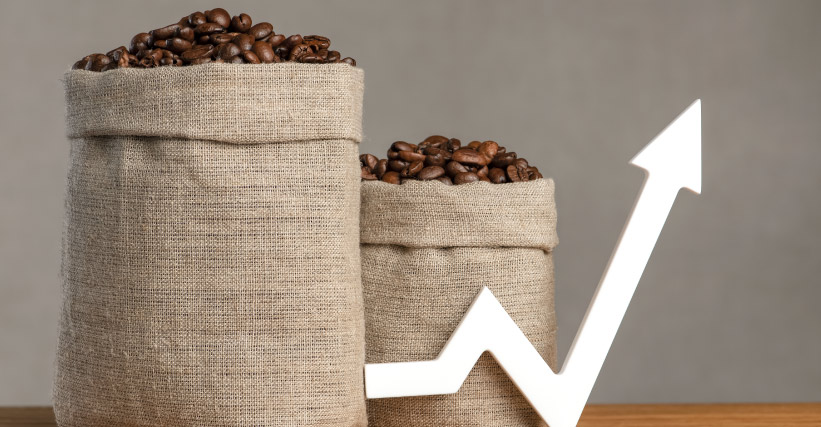 Café premiado - Sacos de juta cheios de grãos de café com seta branca apontando para cima, simbolizando valorização ou crescimento do mercado de café. Além disso, garantir que a página fique apenas com um H1 (título do conteúdo), o que deixamos indicado no arquivo do conteúdo.