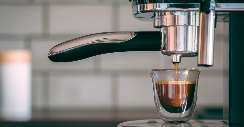 Como escolher cafeteira espresso - Cafeteira espresso preparando uma xícara de café, com foco no fluxo da bebida saindo do porta-filtro e caindo em copo de vidro.