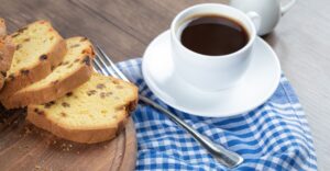 Café com panetone - Xícara de café preto ao lado de fatias de panetone sobre uma toalha xadrez, ilustrando a combinação de café com panetone.