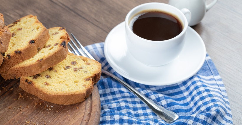 Café com panetone - Xícara de café preto ao lado de fatias de panetone sobre uma toalha xadrez, ilustrando a combinação de café com panetone.