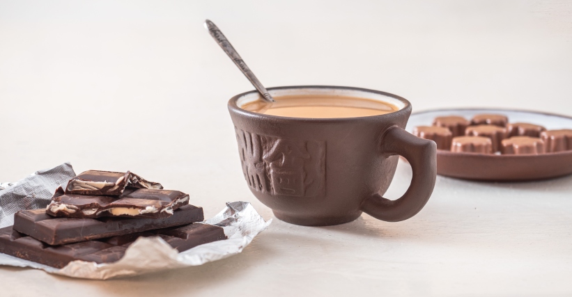Café e Chocolate - Xícara de café cremoso ao lado de barras e bombons de chocolate, em uma composição que destaca a harmonização entre café especial e chocolate.