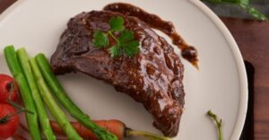 Receitas salgadas com café - Prato com carne ao molho acompanhada de legumes, ilustrando o uso de café como ingrediente em receitas salgadas.